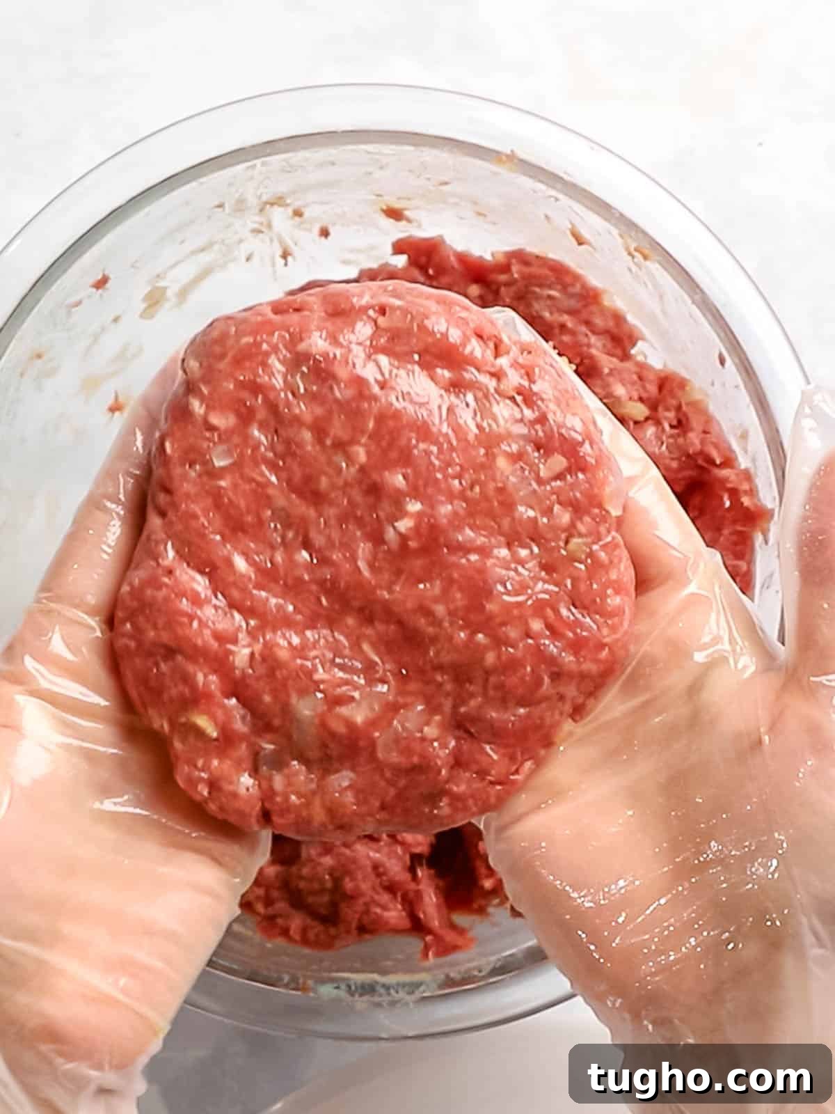 Loco Moco Recipe: Hawaiian Burger with Savory Brown Gravy 7 Ground beef formed into a burger patty that is held with gloved hands.