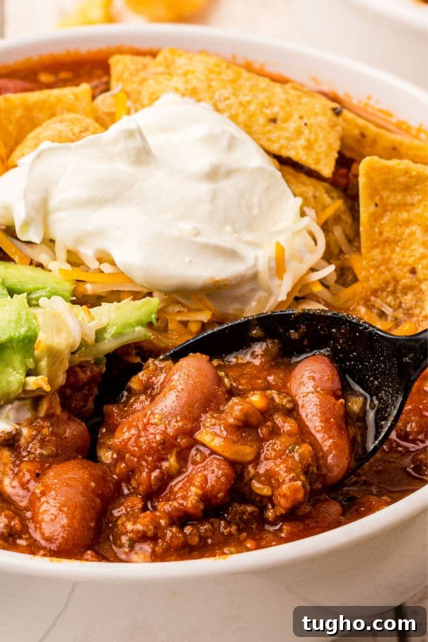 A very close up image of deer chili, with beans in it and corn chips and sour cream.