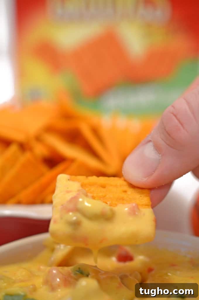 Cheez-It Hot and Spicy Grooves with Tango Sausage Cheese Dip 11 A close up of a person holding a plate of food, with Cheez-It and Cheese